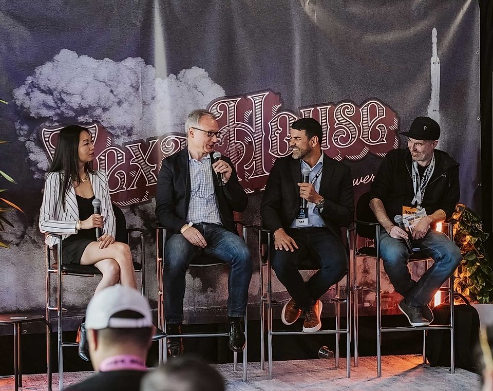 Four speakers on a panel discussing B2B marketing strategies at an event, with a backdrop featuring graphics and branding.