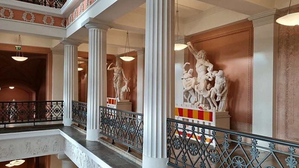 Interior view of a museum featuring classical sculptures, columns, and decorative balconies.