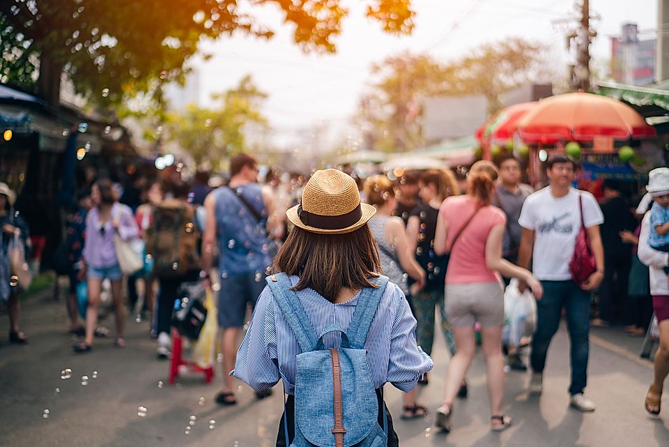 A woman in a hat walks through a busy market street filled with people, shops, and bubbles in a vibrant atmosphere.