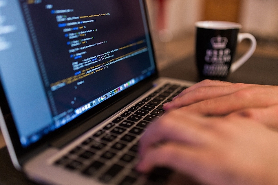 Close-up of hands typing on a laptop displaying code, with a coffee mug in the background.