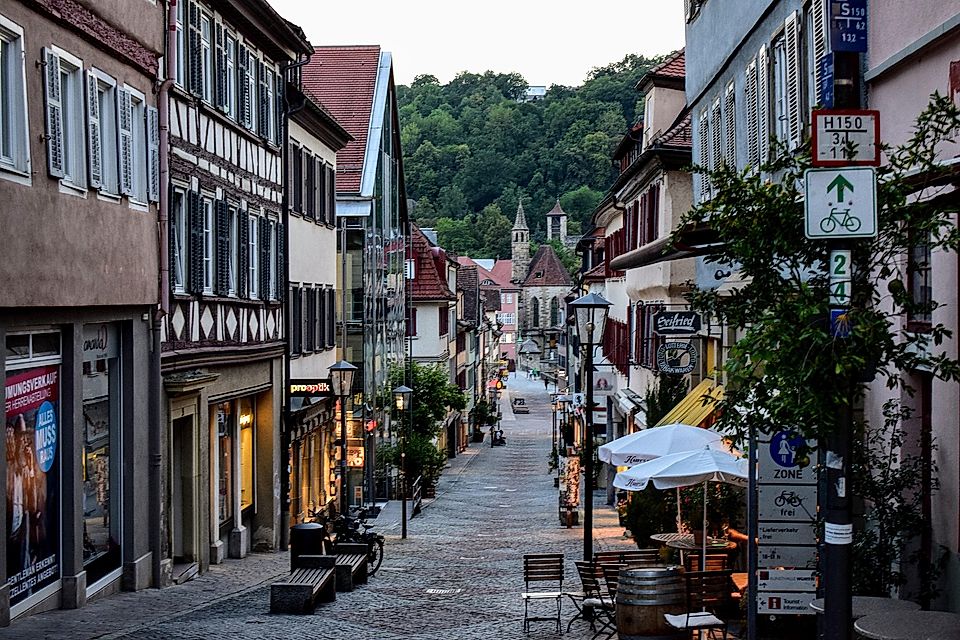 A charming European street lined with traditional buildings, shops, and outdoor seating under a dusk sky.