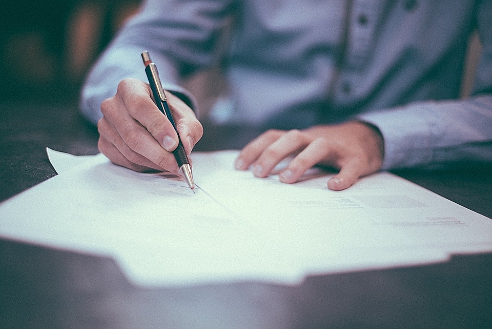 A person writing with a pen on sheets of paper, showcasing a close-up of hands and documents on a desk.