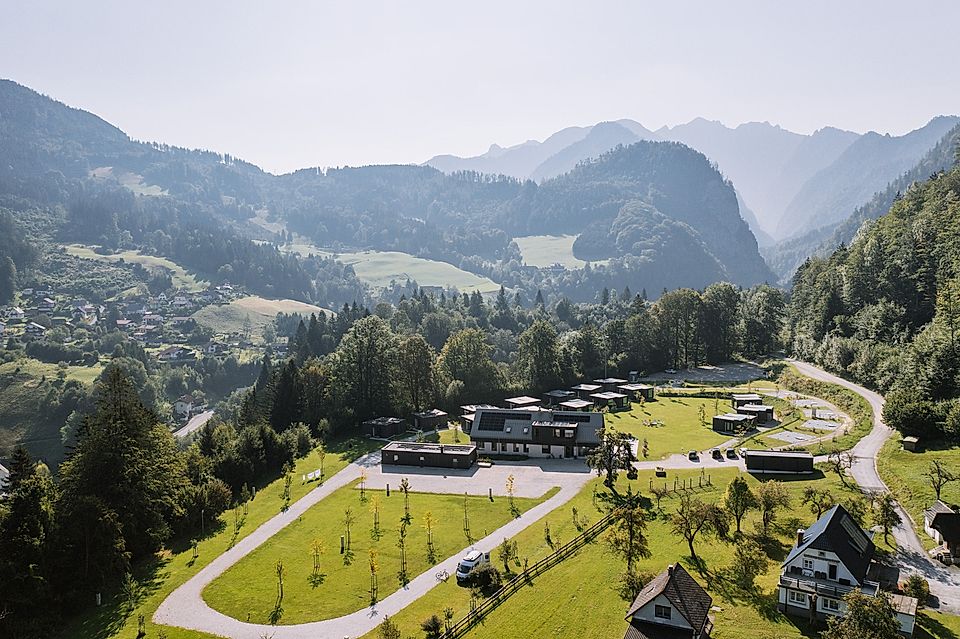 Aerial view of a modern building complex surrounded by lush green hills and mountains on a sunny day.