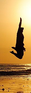 Silhouette of a person jumping against a sunset at the beach, with ocean waves in the background.