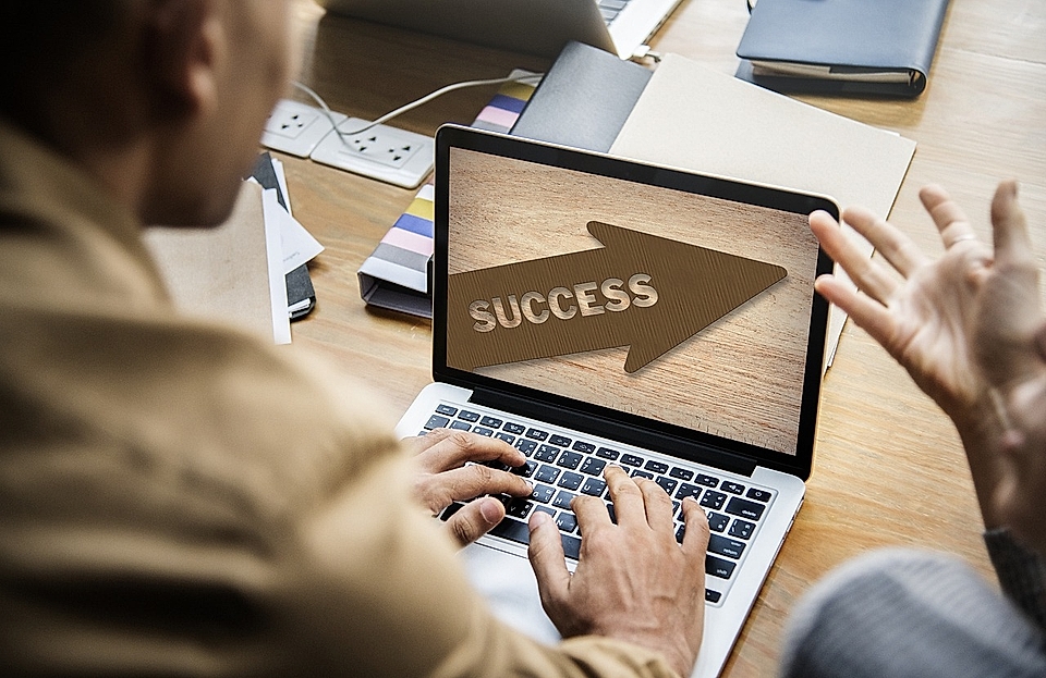 A person working on a laptop displaying the word 'SUCCESS' with an arrow, in a workspace filled with papers.