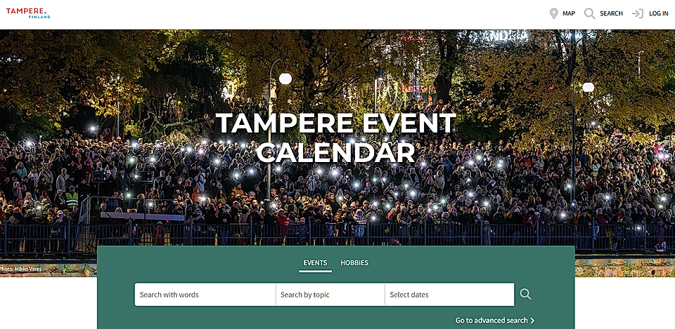 A large crowd at an outdoor event in Tampere, Finland, illuminated by phone lights under autumn trees.