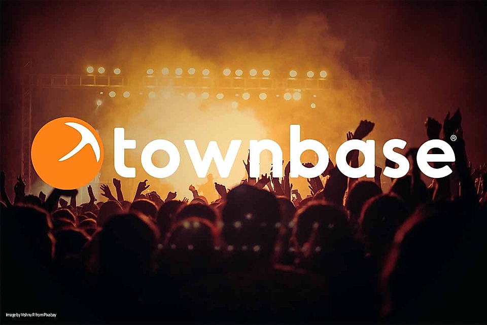 Silhouetted crowd at a concert with bright stage lights and 'townbase' logo in front.