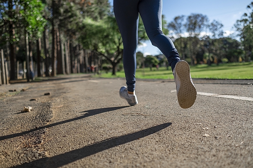 Person jogging on a dirt path surrounded by trees, with sunlight filtering through the leaves.