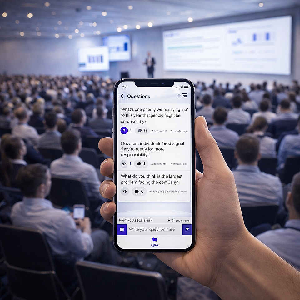 A person holds a smartphone with a Q&A app at a conference. An audience attentively watches a presenter on stage.