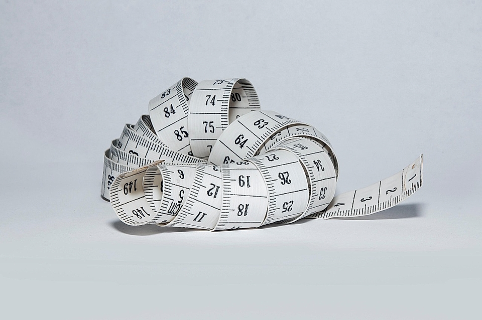 A curled measuring tape with black markings on a white background, showcasing various measurement units.