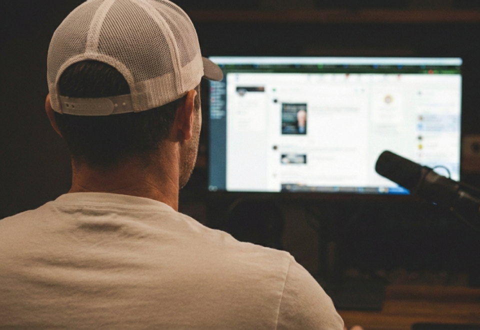 Person sitting at a desk, wearing a white cap, facing a computer screen with social media and content displayed.