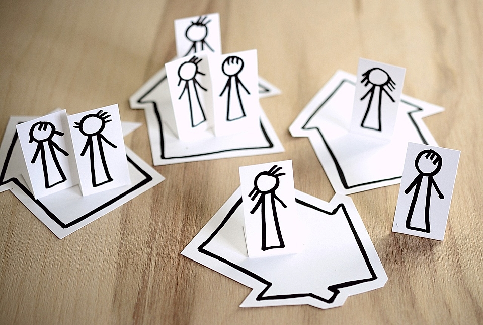 Paper cut-out figures in various poses on arrow-shaped bases, arranged on a wooden surface.