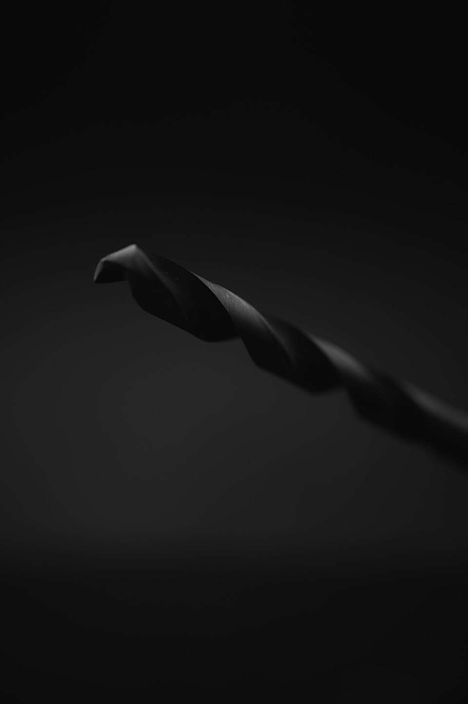 Close-up of a black drill bit on a dark background, showcasing its twisted design and sharp edges.