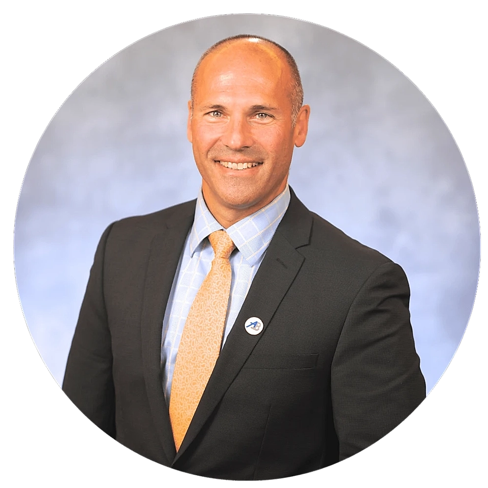Professional headshot of a man in a suit, smiling, with a light blue shirt and orange tie, set against a gray background.