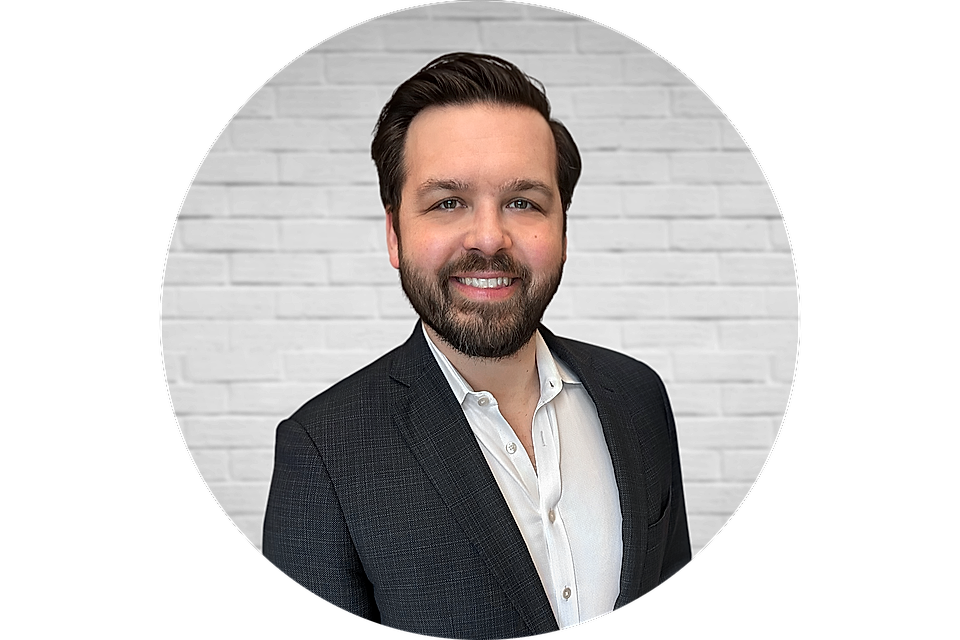 Professional headshot of a smiling man in a suit against a white brick wall