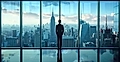 A silhouetted figure stands before large glass windows, overlooking a city skyline featuring the Empire State Building.