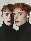 Two red-haired young men in black turtlenecks posed in a minimalist studio portrait.