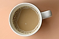 Top-down view of a white mug filled with coffee on a peach background