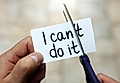 A person cuts a card that says 'I can't do it' with scissors, symbolizing overcoming limitations.