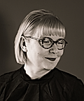 A woman with short, blonde hair and glasses smiles in a monochrome portrait, wearing a dark top.