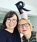 Two women smiling for a selfie, one holding a large letter 'R'.