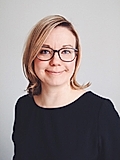 Professional woman with short blonde hair and glasses, smiling against a light gray background.