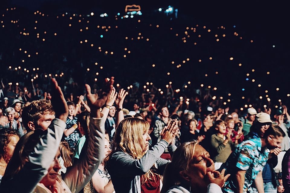 A crowd at a concert with people clapping and holding small lights, creating a lively atmosphere.