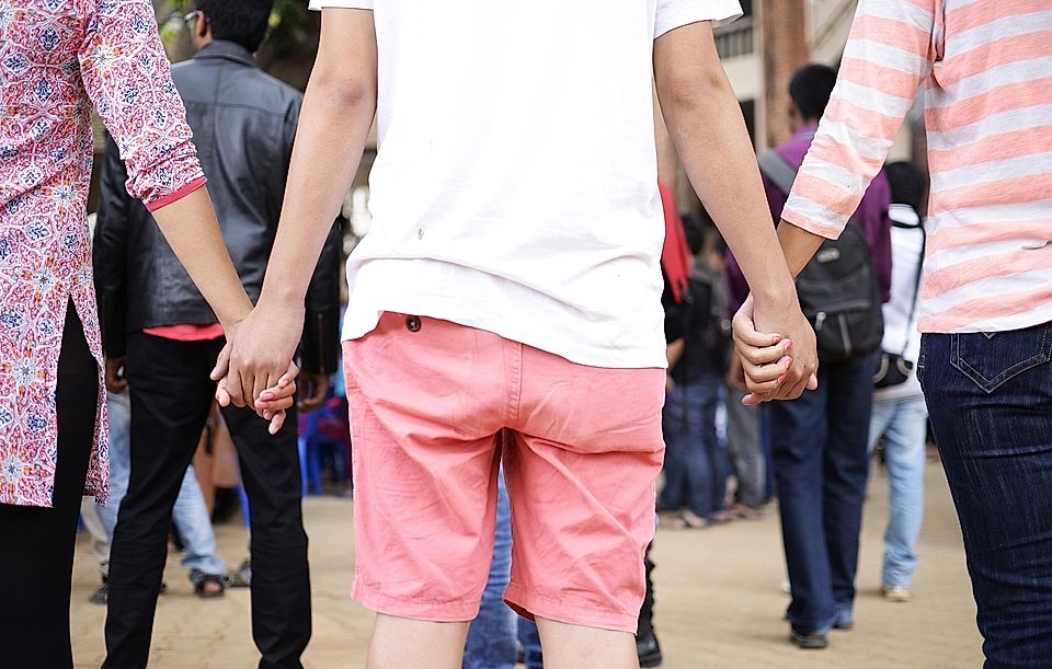 Four people holding hands in a crowd, showcasing unity and togetherness in a lively outdoor setting.