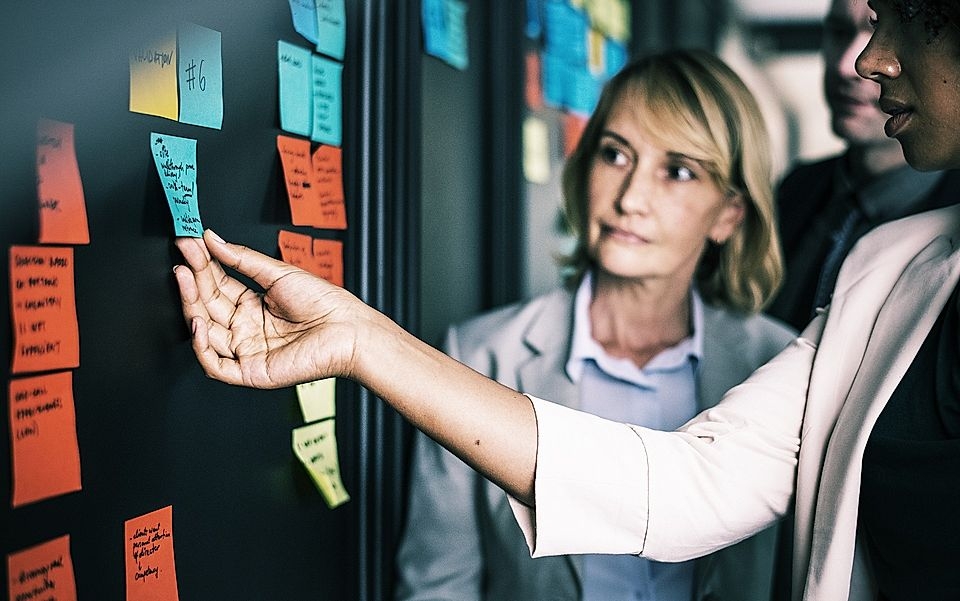 A team collaborates in an office, using sticky notes on a wall for brainstorming ideas and project planning.