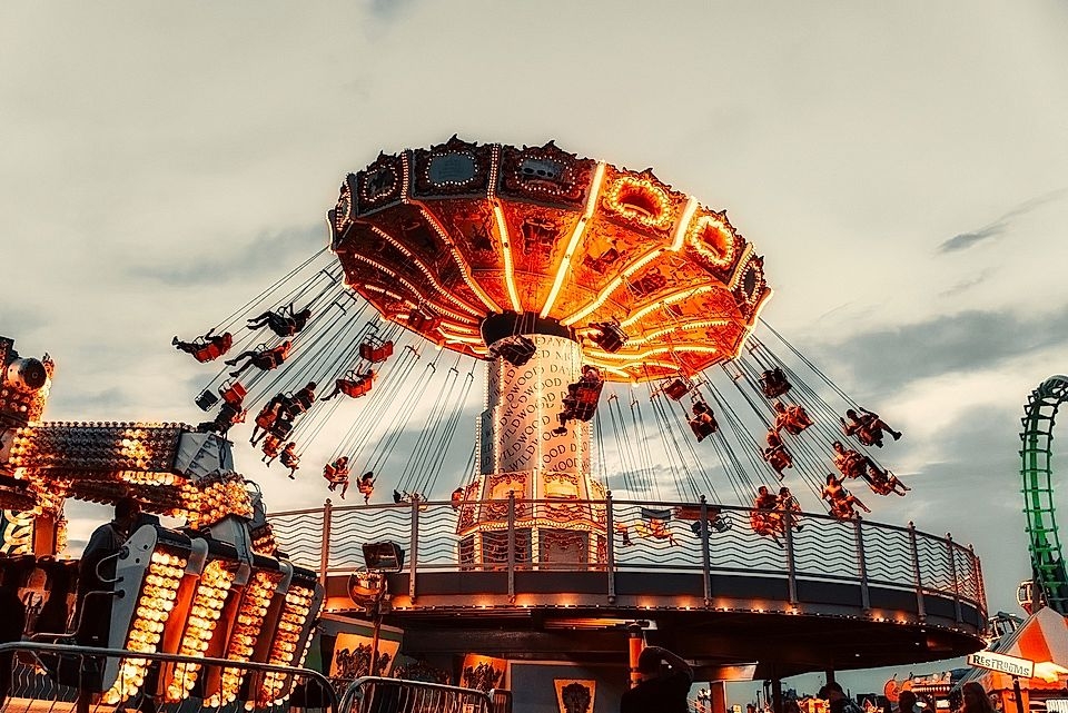 Colorful swing ride at a fair, with riders in motion, illuminated by bright lights against a twilight sky.