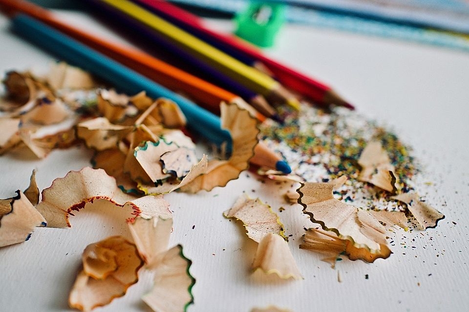 Close-up of colorful pencil shavings and colored pencils on a white surface, with scattered pencil dust.