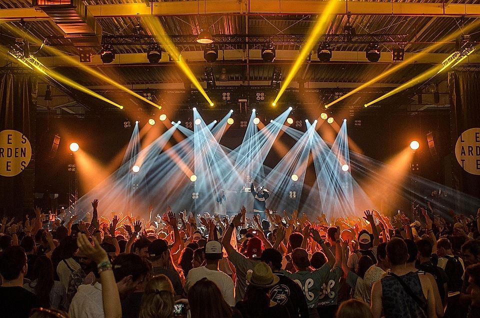 Crowd at a live music concert with raised hands, vibrant stage lights, and a performer on stage.