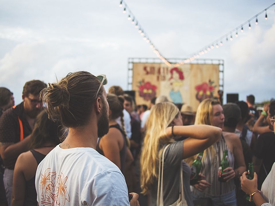 Crowd at an outdoor festival, with people socializing and a backdrop featuring a colorful illustration and lights.