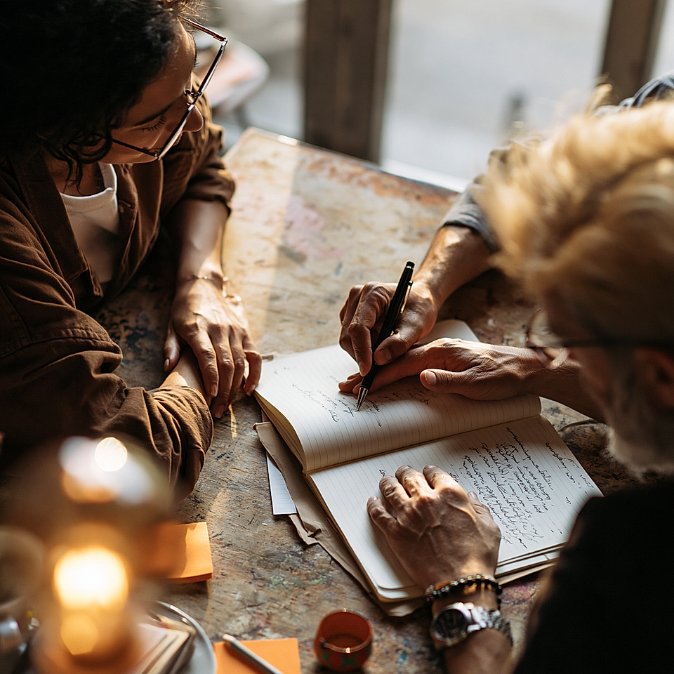 Team collaborating around an open notebook, taking notes at a shared desk