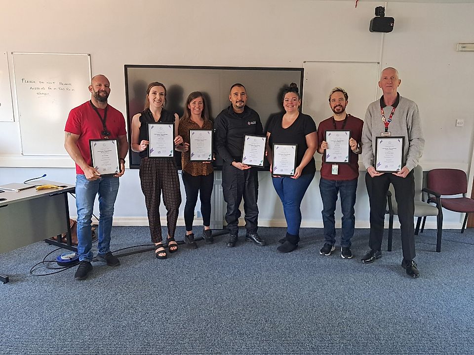 Group of seven people holding framed certificates in a classroom