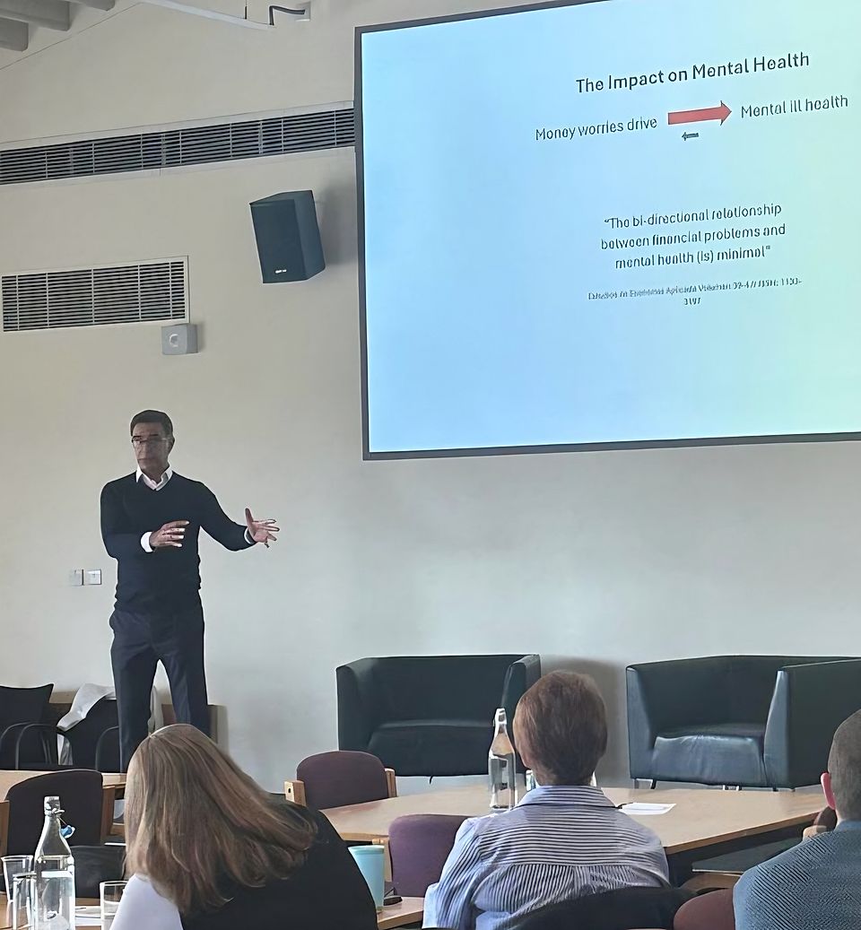 Speaker presenting on mental health and financial stress to an audience in a conference room