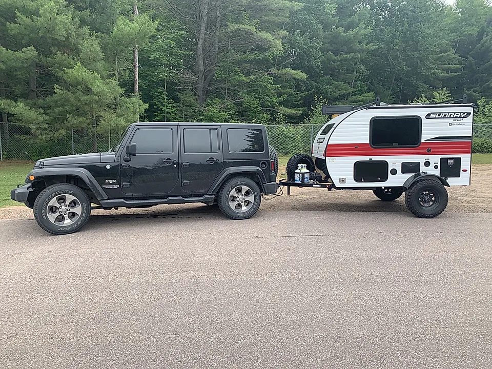 Black Jeep towing a small Sunray camper trailer on a roadside