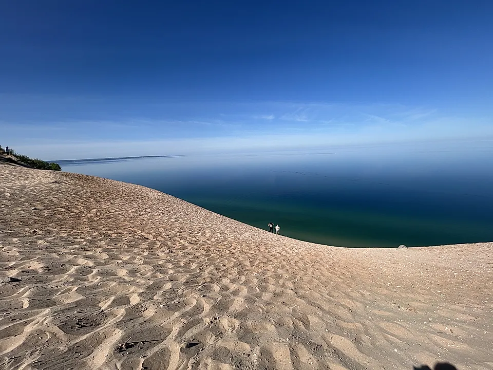Sandy dune overlooking a calm blue lake under a clear sky