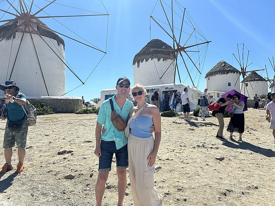 Tourists posing in front of white windmills under a clear blue sky