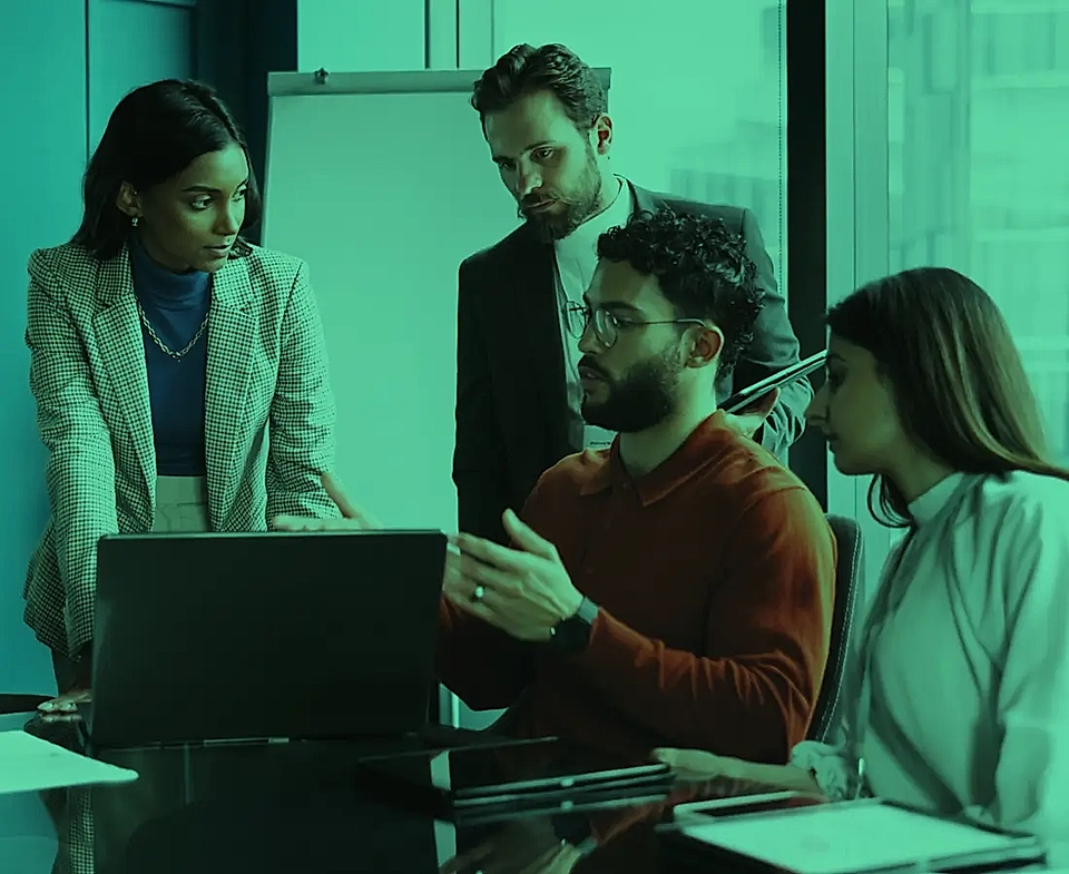 Team meeting in a conference room with four individuals discussing a laptop screen.