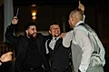 Three men in formal attire celebrating and dancing at a night event