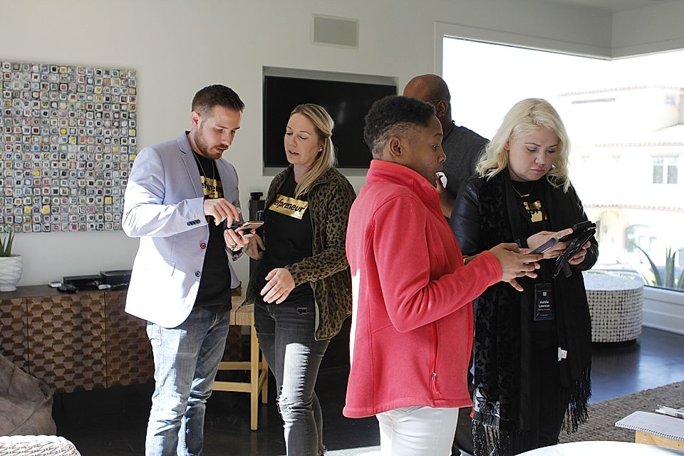Group of people standing indoors, looking at smartphones in a bright living room